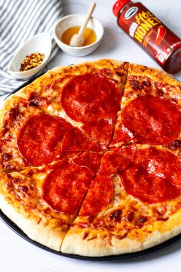 Close-up of sliced hot honey pepperoni pizza with red pepper flakes and hot honey