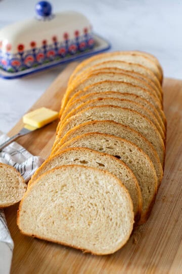 Homemade honey wheat sandwich bread sliced on a cutting board with butter