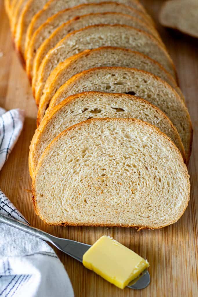 Close-up of sliced honey wheat sandwich bread showing the soft crumb with butter on the side