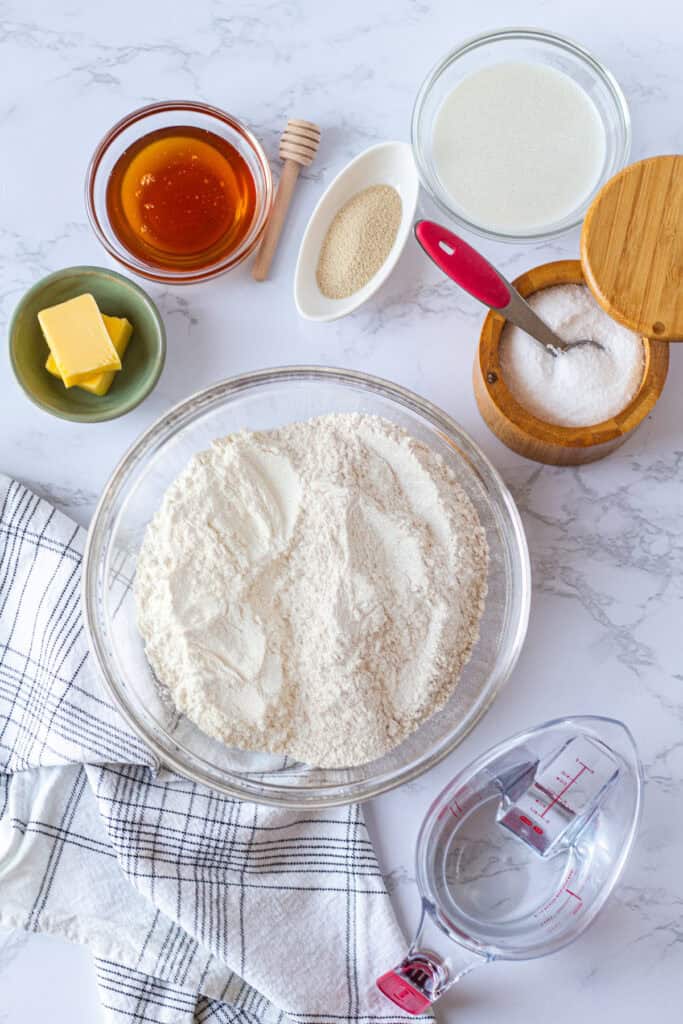 Ingredients for homemade honey wheat sandwich bread, including flour, honey, milk, butter, yeast, salt, and water