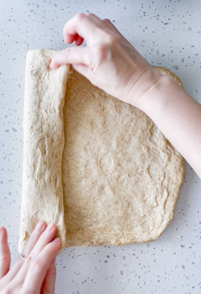 Folding one side of honey wheat bread dough toward the center while shaping a sandwich loaf