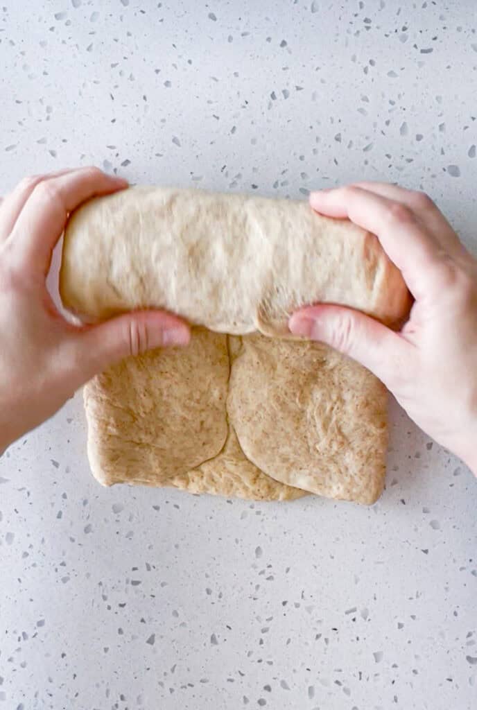 Rolling folded honey wheat bread dough into a loaf before placing it in the pan