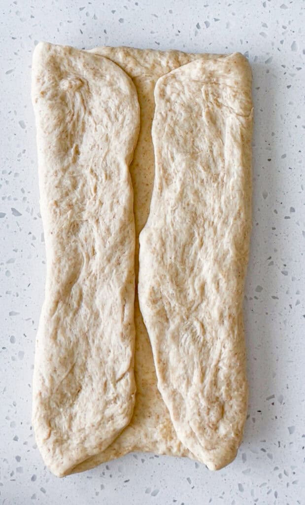 Both sides of honey wheat bread dough folded toward the center before rolling into a loaf