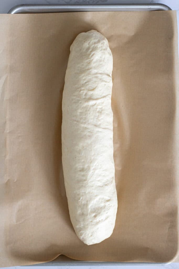 French bread dough shaped into a long loaf on a parchment-lined baking sheet.