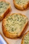 Close-up of a toasted slice of garlic bread topped with melted garlic-Parmesan butter and parsley.