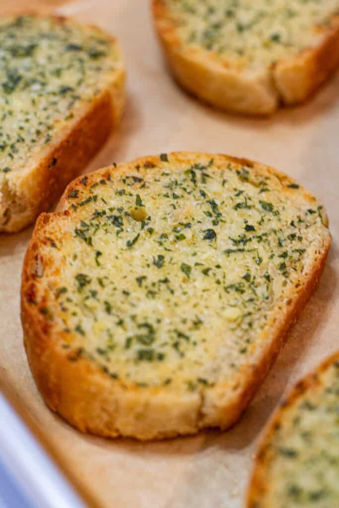Close-up of a toasted slice of garlic bread topped with melted garlic-Parmesan butter and parsley.