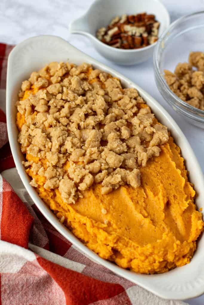 Creamy sweet potato filling in a white oval baking dish, partially covered with brown sugar crumble topping.