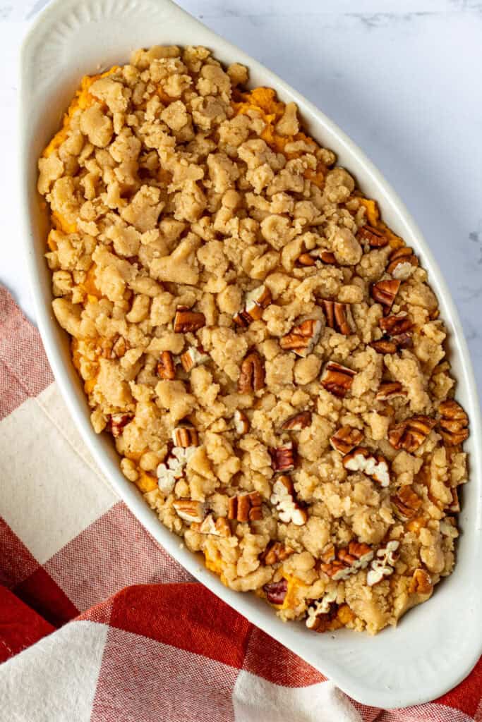 Overhead view of sweet potato casserole in a white oval dish with crumble topping and chopped pecans sprinkled over one side.