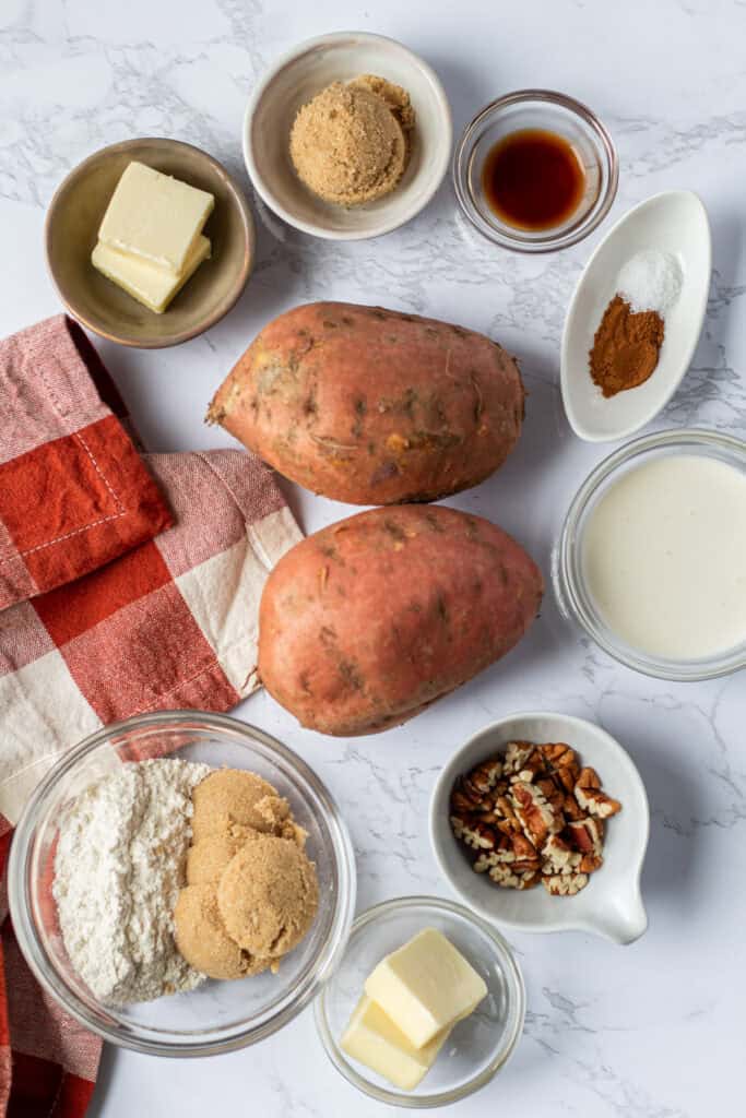 Overhead arrangement of sweet potatoes, butter, brown sugar, cream, vanilla, cinnamon, flour, salt, and chopped pecans.