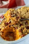 Close-up of a spoon lifting creamy sweet potato casserole topped with golden brown crumble and chopped pecans.