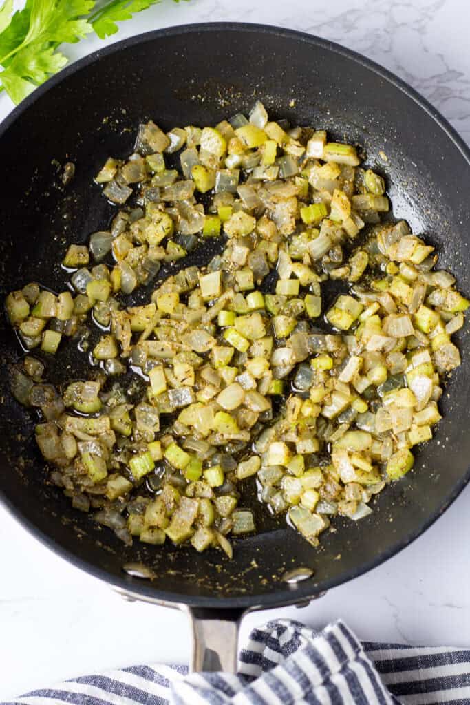 Finely diced onion and celery sautéed with butter, garlic, and dried herbs in a black skillet.