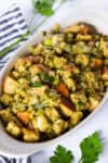 Homemade Thanksgiving stuffing with golden bread cubes, onion, celery, and parsley in a small white oval casserole dish.
