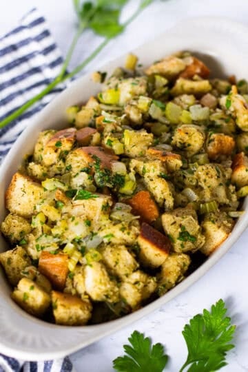 Homemade Thanksgiving stuffing with golden bread cubes, onion, celery, and parsley in a small white oval casserole dish.