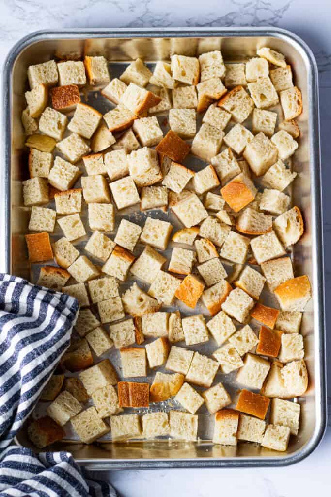 Half-inch bread cubes spread in a single layer on a metal baking sheet, ready to dry in the oven.