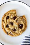 Large chocolate chip cookie with a bite taken out, topped with melted dark chocolate and flaky sea salt