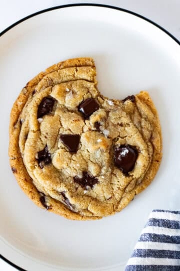 Large chocolate chip cookie with a bite taken out, topped with melted dark chocolate and flaky sea salt